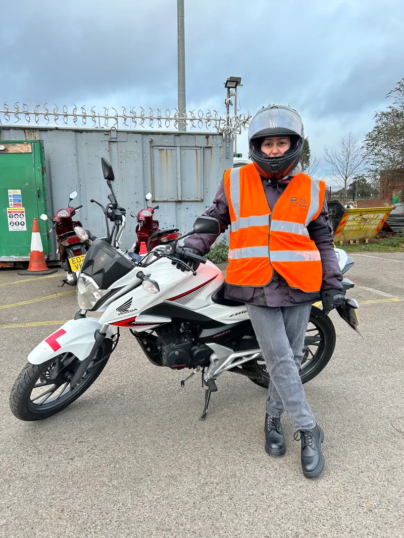A learner in an orange vest next to a white motorbike with L plates