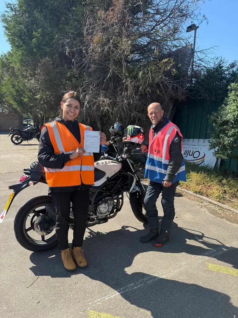 A student and instructor with a pass certificate next to a motorbike