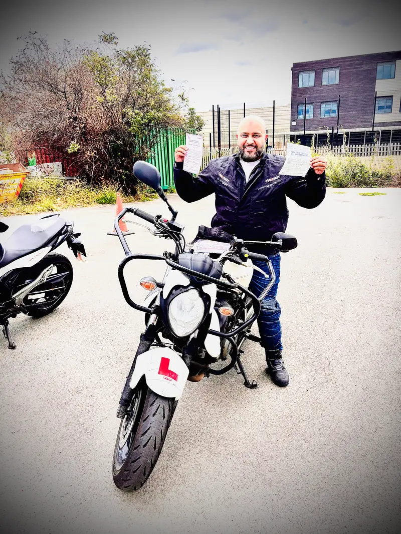 A smiling student holding up a certificate next to a learner motorbike