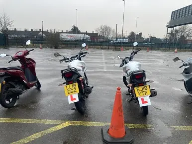 Learner scooters and motorbikes lined up behind a cone on a wet day