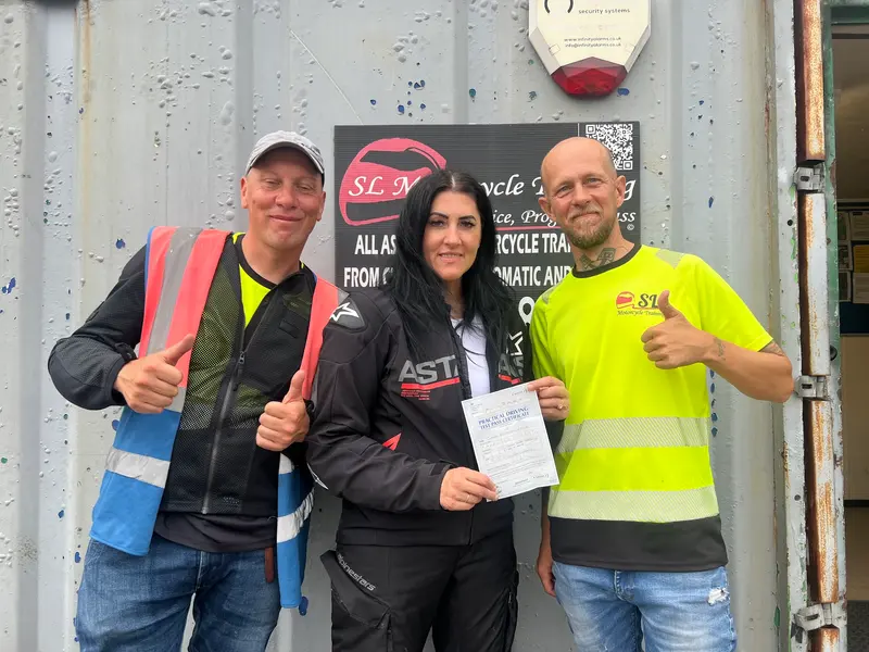 A student and two instructors with a certificate in front of the SL sign
