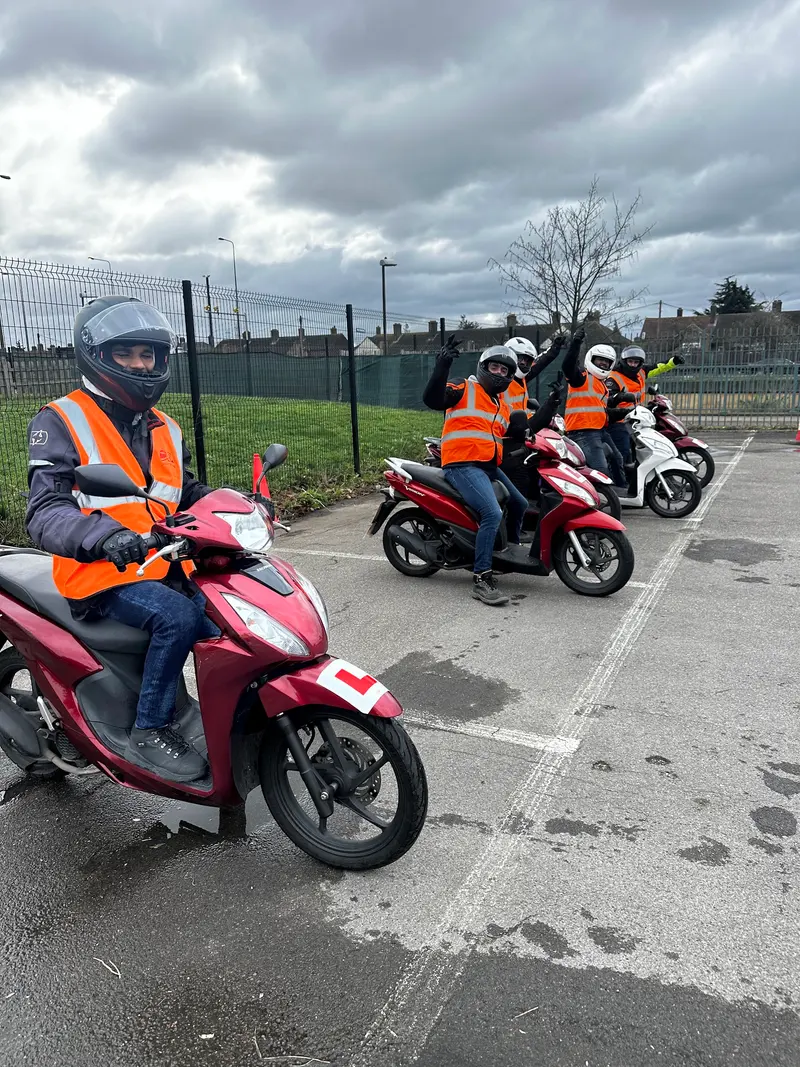 A learner on a red scooter with other learners lined up behind