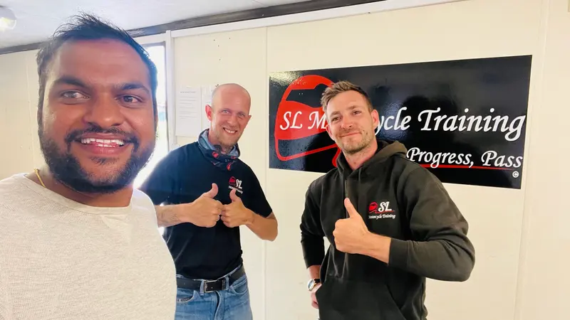 A student and two instructors giving a thumbs up in front of the SL sign