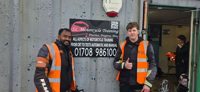 Two students in hi-vis vests giving a thumbs up in front of the SL Motorcycle Training sign