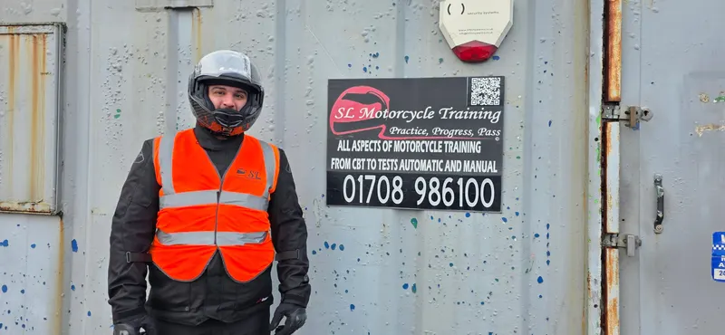 A rider in a helmet and orange SL vest in front of the SL sign