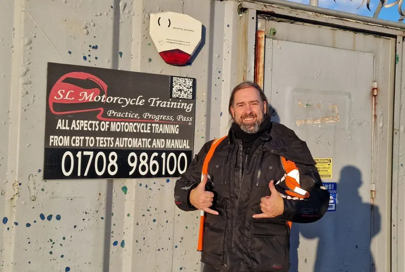 A smiling rider in motorcycle kit in front of the SL sign
