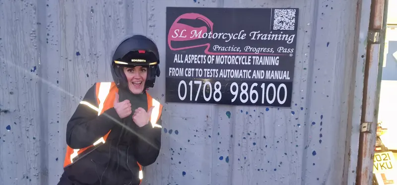 A rider in a helmet and hi-vis jacket giving two thumbs up in front of the SL sign